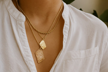 A macro close-up of the handmade freeform 14K gold-filled pendants, emphasizing their unique, textured silhouettes and high-polish finish.
