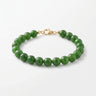 A studio product shot of a women's 8mm natural green jade bead bracelet with a 14k gold-filled lobster clasp.  