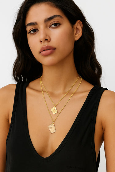 A portrait-view lifestyle shot of a model wearing two layered 14K gold-filled pendants, showcasing the organic shapes and the refined drape of the box chains.
