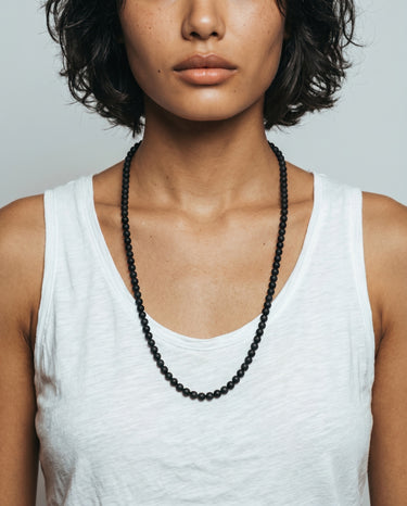 Woman wearing a matte black onyx bead necklace against a neutral background