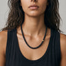 Woman wearing a black onyx beaded necklace with one single off-centered 14k gold-filled accent bead  against a neutral background.