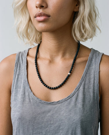 Woman wearing a black onyx beaded necklace with one single off-centered sterling silver accent bead  against a neutral background.