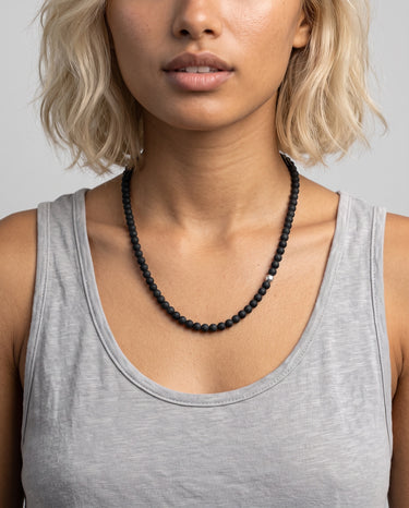 Woman wearing a black onyx beaded necklace with one single off-centered silver accent bead  against a neutral background.