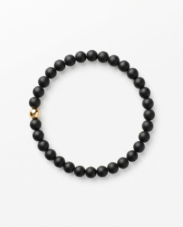 A studio product shot of a women's 6mm matte black onyx bead bracelet featuring a single 14K gold-filled accent bead on a white background.