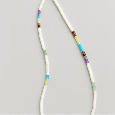 The Multi-Gemstone heishi bead necklace laid out in a fluid S-curve shape against a plain background, illustrating the suppleness of the chain and the full spectrum of colors in the gemstone curation.
 design