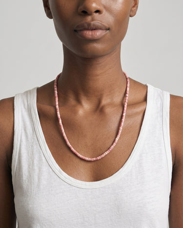 woman wearing a white tank top and pink rhodonite heishi beaded necklace against a plain background