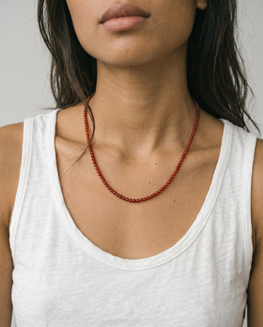woman with a white tank top wearing 4mm red agate beaded necklace against a plain background