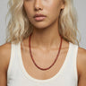 Woman with an off-white tank top wearing a red agate beaded necklace against a neutral background