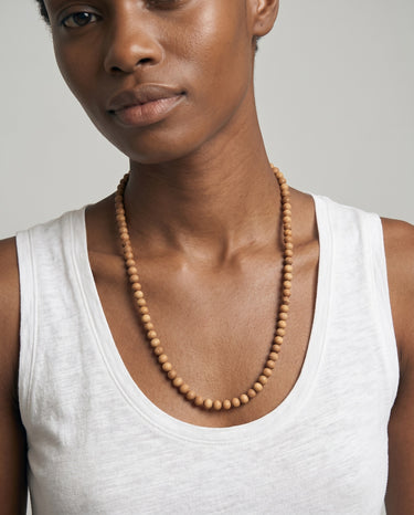 Woman wearing an 8mm sandalwood long beaded necklace paired with a tank top on a light gray background. 