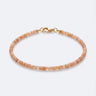 A studio product shot of a women's 2mm natural faceted golden sunstone cube bead bracelet with a 14K gold-filled clasp, highlighting the shimmering peach tones and delicate light-catching facets.
