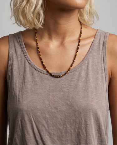 A woman wearing a 4mm tiger's eye round bead necklace with a taupe tank top for an editorial, sophisticated look.