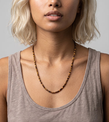 A woman wearing a 4mm tiger's eye round bead necklace, showcasing the warm tones of the stones against a white tank top for an editorial, sophisticated look.