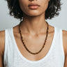 Person wearing a 6mm tiger's eye beaded necklace with a plain background