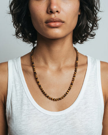 Person wearing a 6mm tiger's eye beaded necklace with a plain background