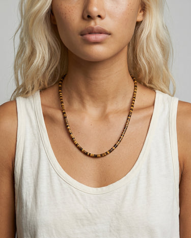 Woman with an off-white t-shirt wearing a tiger's eye beaded necklace with a plain gray background
