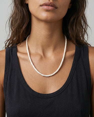 woman with a black tank top wearing a white heishi necklace on a gray background