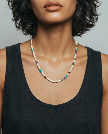 A studio shot of a female model wearing a colorful mixed heishi bead necklace against a neutral background