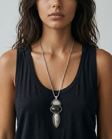 Front view of a handcrafted three-stone Fossato pendant with individually shaped sterling silver bezels and black oxidized channels surrounding the gemstones.