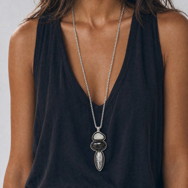 Front view of a handcrafted three-stone Fossato pendant with individually shaped sterling silver bezels and black oxidized channels surrounding the gemstones.