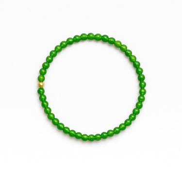 Product shot of a 4mm round green jade beaded stretchy bracelet with one 14k gold-bead accent on a white background