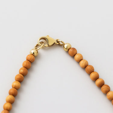 Close-up shot of the 14K gold-filled clasp for a 4mm round golden tan color sandalwood bead necklace against a neutral background