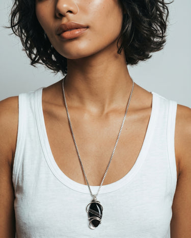 Woman modeling a Black Obsidian gemstone pendant with intricate sterling silver wire wrapping, suspended from a long silver chain.