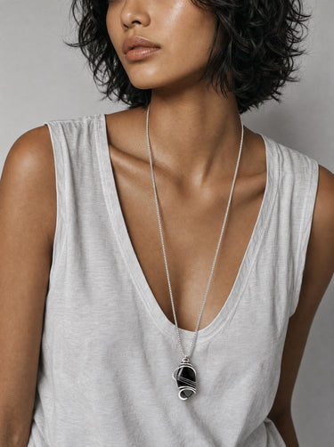 Woman wearing a long silver chain necklace with a polished Black Obsidian pendant, hand-wrapped in sculptural sterling silver wire.