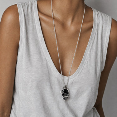 Woman wearing a long silver chain necklace with a polished Black Obsidian pendant, hand-wrapped in sculptural sterling silver wire.