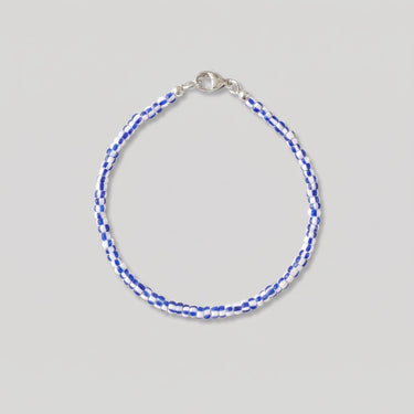 A studio product shot of a women's 2-3mm blue and white african chevron glass bead bracelet with a sterling silver lobster clasp on a light gray background.