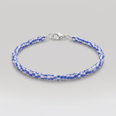 A beaded bracelet with alternating blue and white African chevron glass beads, finished with a silver lobster clasp, shown on a light gray background.