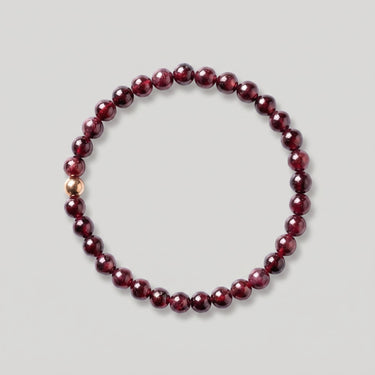 A beaded stretch bracelet made of round deep red garnet beads with a single 14k gold-filled accent bead, displayed on a neutral light gray background.