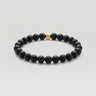 A product shot of beaded stretch bracelet made of matte black round beads with a single polished 14k gold-filled accent bead, shown on a light gray background.