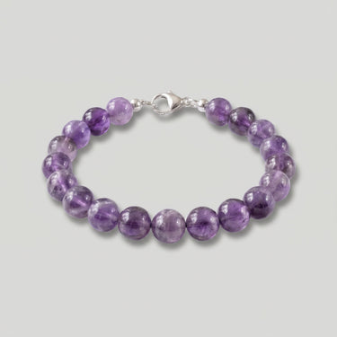 A studio product shot of a women's 8mm natural amethyst bead bracelet with a sterling silver lobster clasp on a light gray background.