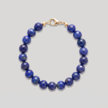 A studio shot of a women's 8mm natural lapis lazuli bead bracelet with a 14K gold-filled lobster clasp, highlighting the deep royal blue gemstone tones and high-polish finish.