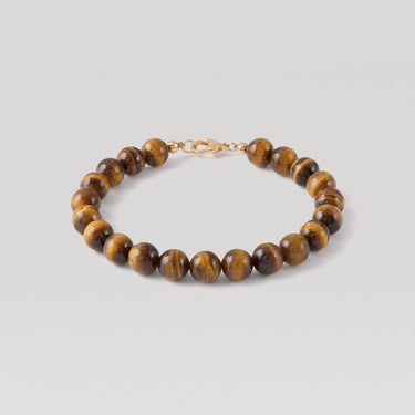 A beaded bracelet made of polished brown and gold tiger's eye beads with a small gold clasp, displayed on a light gray background.