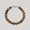 A tigers eye beaded bracelet made of polished tiger's eye round beads with a silver lobster clasp, displayed on a neutral light gray background.
