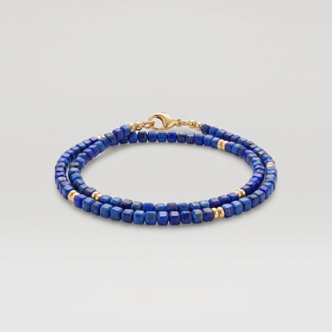 A studio product shot of a women's 3mm natural faceted lapis lazuli cube wrap bracelet featuring 14K gold-filled bead accents, highlighting the vibrant royal blue gemstones and elegant layered design.