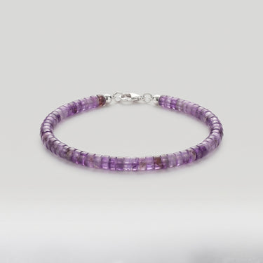 A beaded bracelet made of small amethyst heishi gemstone beads with a silver clasp, on a light gray background.