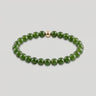 A product shot of a beaded stretch bracelet made of polished dark green round beads with a single small gold accent bead, displayed on a light gray background.