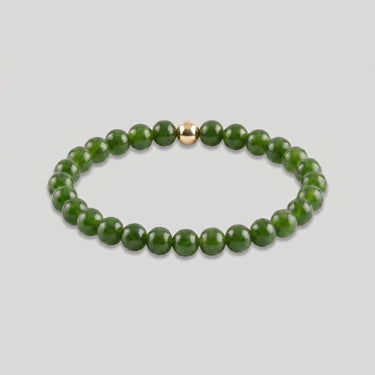A product shot of a beaded stretch bracelet made of polished dark green round beads with a single small gold accent bead, displayed on a light gray background.