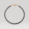 A beaded bracelet made of black faceted square beads with a polished gold-tone lobster clasp, shown on a light gray background.