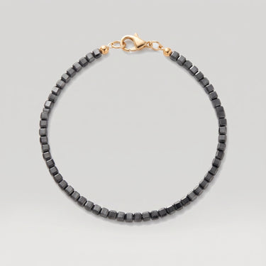 A beaded bracelet made of black faceted square beads with a polished gold-tone lobster clasp, shown on a light gray background.