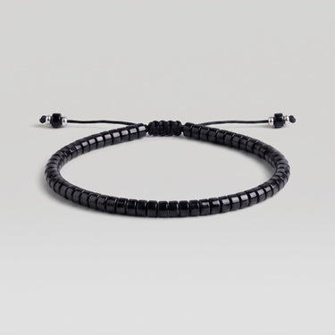 A black beaded bracelet with a sliding knot closure, shown on a neutral light gray background.
