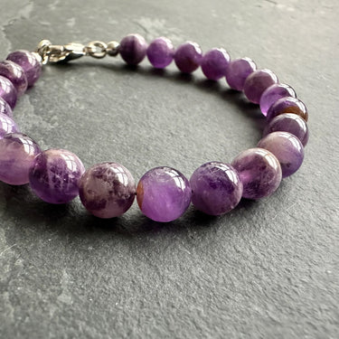 8mm amethyst bead bracelet for men laying on dark stone