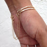 A lifestyle shot of a model wearing a stack of two handcrafted 14K gold-filled cuff bracelets featuring a delicate safety chain, showcasing a modern, layered luxury look.
